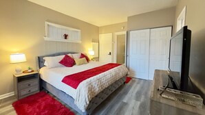 Ein Schlafzimmer mit einem Bett, Nachttischen, einem roten Teppich, einem Fernseher und einem Kleiderschrank.
