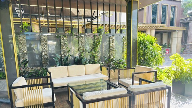 Un espace de détente extérieur moderne, avec un canapé et des fauteuils, entouré de plantes et d’un mur en pierre.
