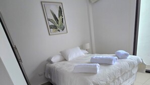 Ein ordentlich bezogenes Bett mit weißen Leinen und Handtüchern, eine Nachttischlampe und ein gerahmtes Bild mit einer Pflanze an der Wand.