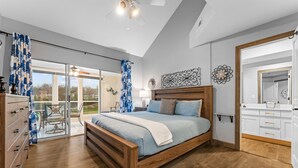 A bedroom with a wooden bed, a glass door leading to a balcony, and a kitchen area with white cabinets. - Gorgeous Golf Views Condo in the heart of Branson (sleeps 8) (Branson)
