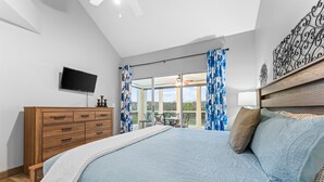 A bedroom with a large bed, a wooden dresser, a flat-screen TV, and a balcony with blue curtains. - Gorgeous Golf Views Condo in the heart of Branson (sleeps 8) (Branson)