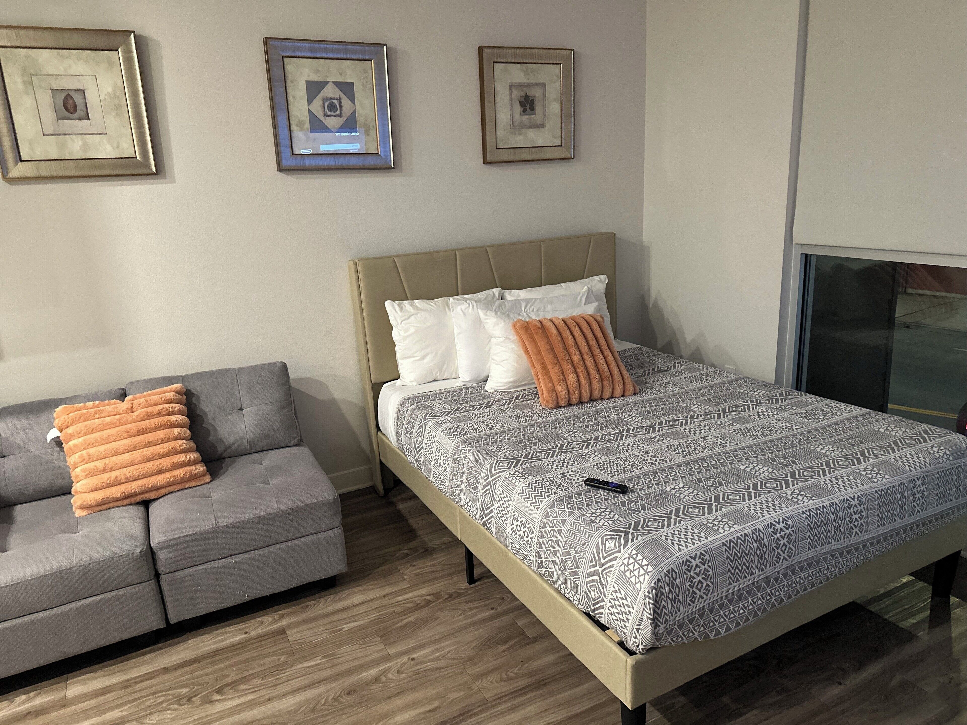 Un dormitorio con una cama, un sofá gris y tres cuadros en la pared.