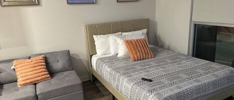 Un dormitorio con una cama, un sofá gris y tres cuadros en la pared.