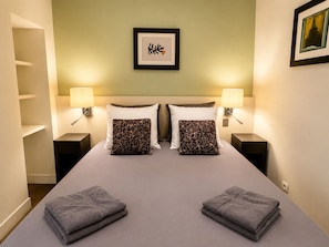 A hotel room with a large bed, two pillows, two nightstands, two lamps, a framed picture on the wall, and two folded towels on the bed.