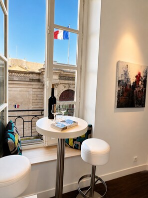 A room with a table, two white stools, a bottle, and two glasses on the windowsill.