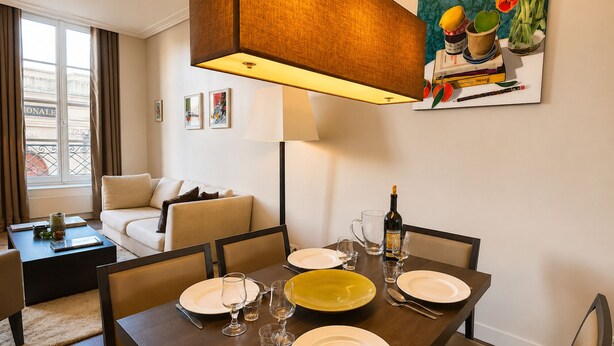 Un coin repas avec une table dressée pour quatre personnes, une bouteille de vin et un tableau accroché au mur.