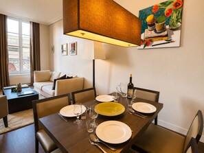Uma sala de jantar com uma mesa posta para quatro pessoas, uma garrafa de vinho e um quadro na parede.