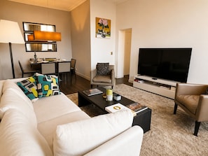 A living room with a sofa, coffee table, TV, and a dining area with chairs and a table.