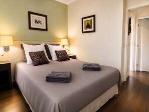 Cama bem arrumada com almofadas, duas luminárias na parede e quadros decorativos.