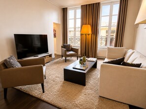 A modern living room with a flat-screen TV, two sofas, a coffee table, and a large window with curtains.