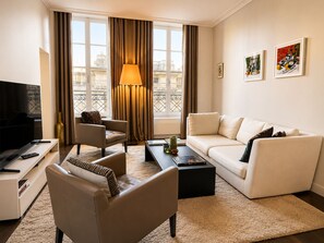 Uma sala de estar moderna com sofá, poltrona, mesa de centro, televisão e obras de arte nas paredes.