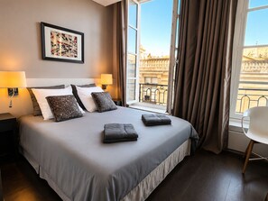 A hotel room with a large bed, two bedside lamps, a framed picture on the wall, and a view of the city through the window. - L'appartement des Archives (Paris)