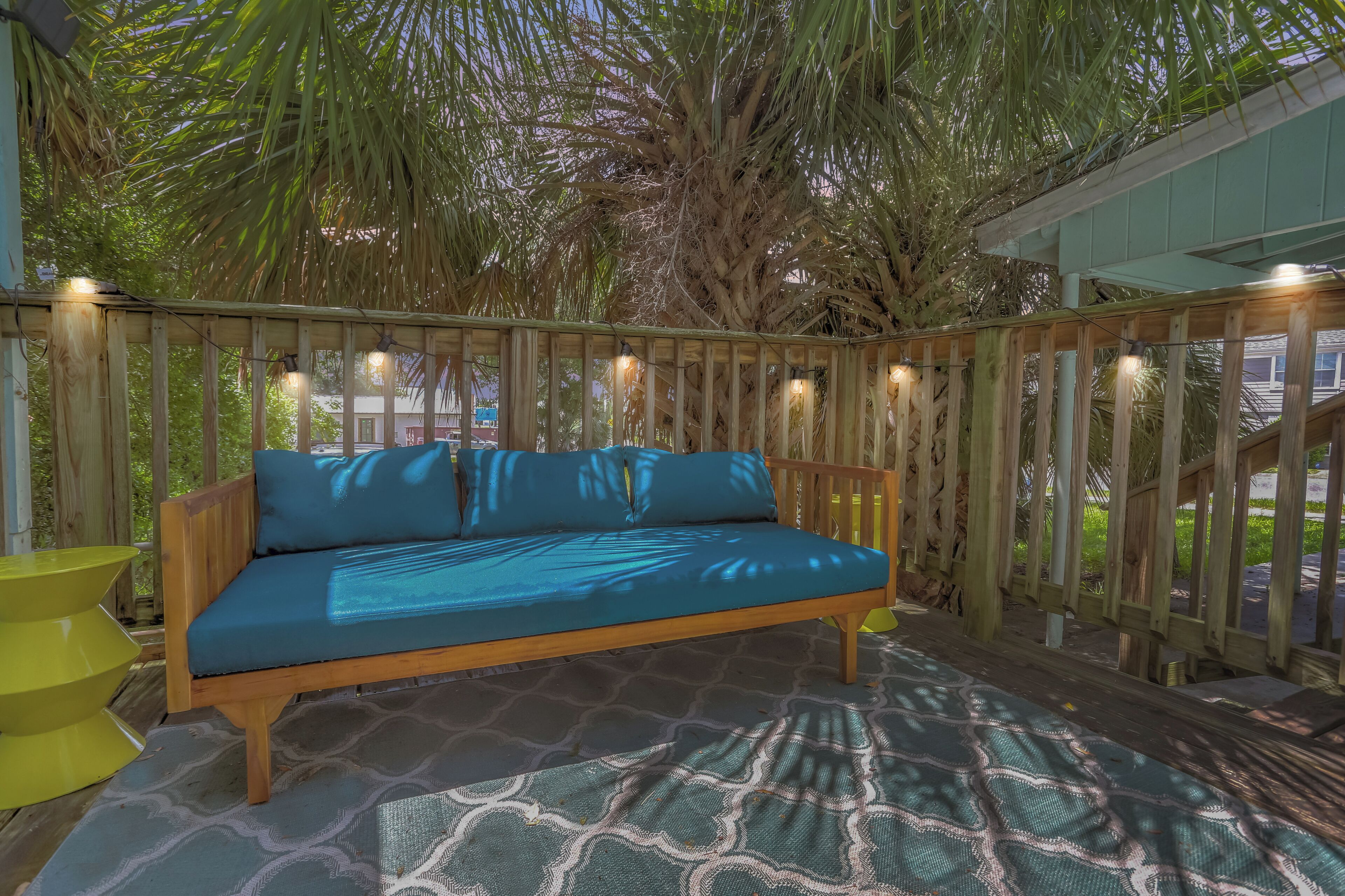 Eine Holzterrasse mit einem blauen Sofa, einem gemusterten Teppich und Lichterketten.