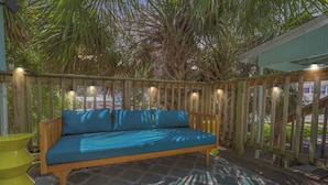 A wooden deck with a blue sofa, a patterned rug, and string lights.