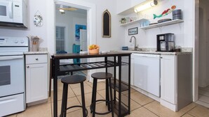 A compact kitchen with white cabinets, a black bar stool, a coffee machine, and a microwave.