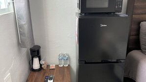 A compact kitchenette with a black refrigerator, a microwave, a coffee maker, and a small wooden table with a remote control and water bottles. - Molinos House 3 (Santa Isabel)