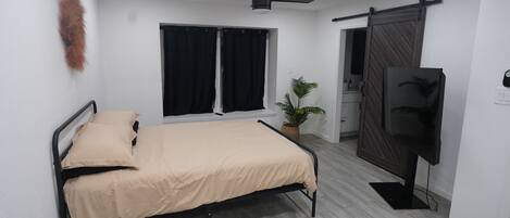 Ein Schlafzimmer mit einem Bett, einem Deckenventilator, einem Fernseher und einer Schiebetür.