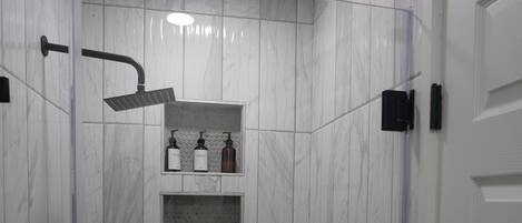 A modern shower area with a glass enclosure, a built-in shelf with toiletries, and a handheld showerhead.