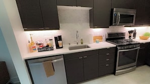 A modern kitchen with dark cabinets, a stainless steel sink, a microwave, and a stove. - Cozy Walk of Fame gem. 1b1b, Free Parking, Pool, Private Balcony, WiFi & more! (Los Angeles)