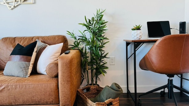 A living room with a brown leather sofa, a brown leather chair, a small table with a laptop, a potted plant, and a woven basket. - Cozy Walk of Fame gem. 1b1b, Free Parking, Pool, Private Balcony, WiFi & more! (Los Angeles)