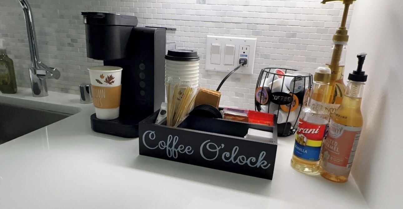 Eine Küchenarbeitsplatte mit Kaffeemaschine, Kaffeetasse, Kaffeemühle und verschiedenen Kaffeekapseln.