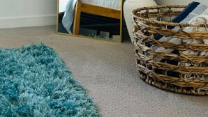 A bedroom with a large mirror, a bed with a white duvet, a blue rug, a wicker basket, and a vase with pampas grass. - Cozy Walk of Fame gem. 1b1b, Free Parking, Pool, Private Balcony, WiFi & more! (Los Angeles)