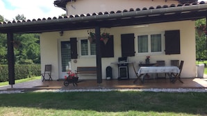 Une terrasse couverte avec une table et des chaises, un banc, un barbecue et une plante en pot.