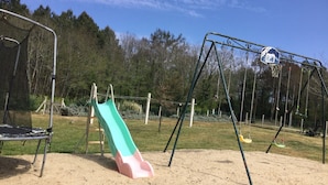 Une aire de jeux avec un toboggan, des balançoires et un panier de basket.