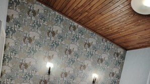 Une chambre avec un plafond en bois, un lit recouvert d’une courtepointe blanche, deux tables de chevet et un papier peint à motifs floraux.