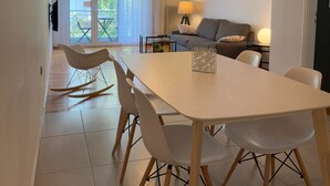 A modern living room with a sofa, a dining table with chairs, and a balcony with a view.