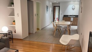A modern living room with a wooden floor, a sofa, a glass coffee table, and a dining area with a table and chairs.