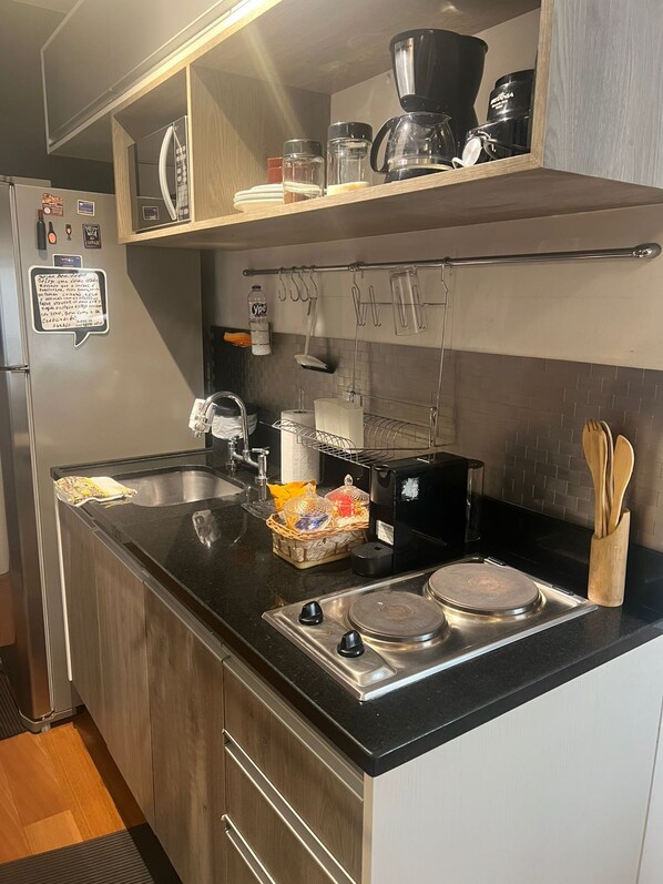 A compact kitchen with a black countertop, stainless steel appliances, and wooden cabinets.
