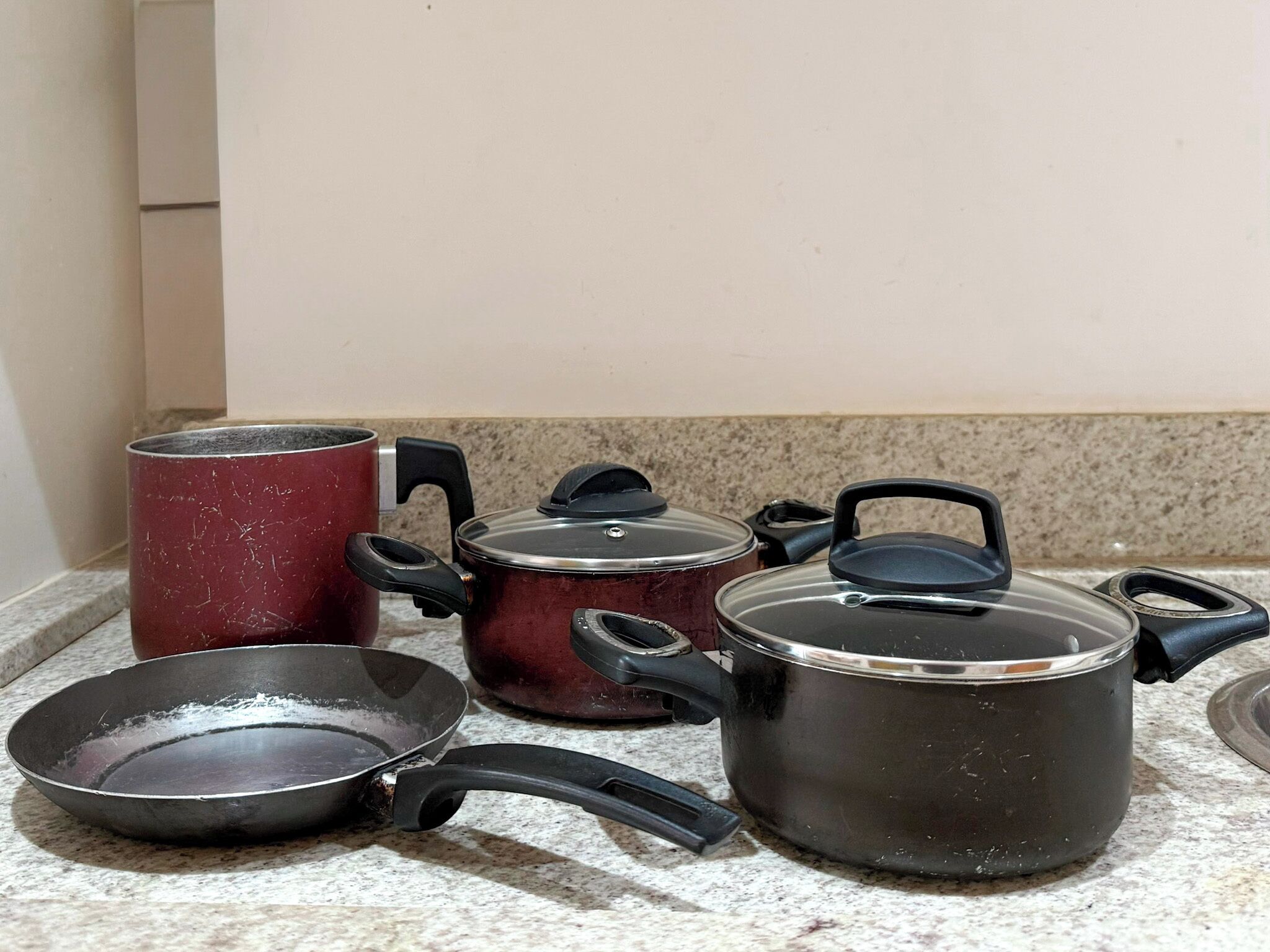 Una encimera de cocina con diferentes utensilios de cocina, incluyendo una sartén, una olla roja y dos ollas negras con tapa.