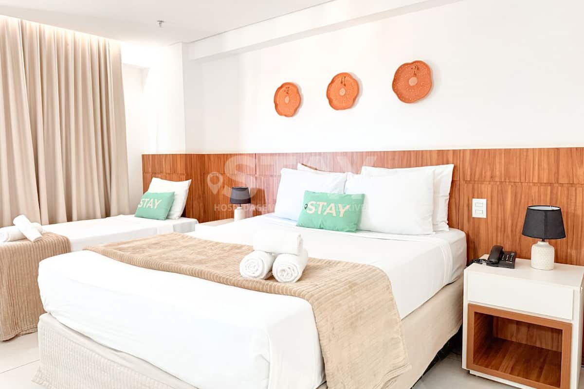 A hotel room with two beds, a wooden headboard, a nightstand with a lamp, and a wall-mounted phone.