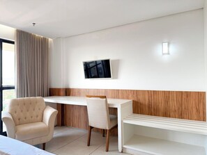 Espaço de escritório moderno com escrivaninha, duas cadeiras, TV fixada na parede e vista para o exterior.