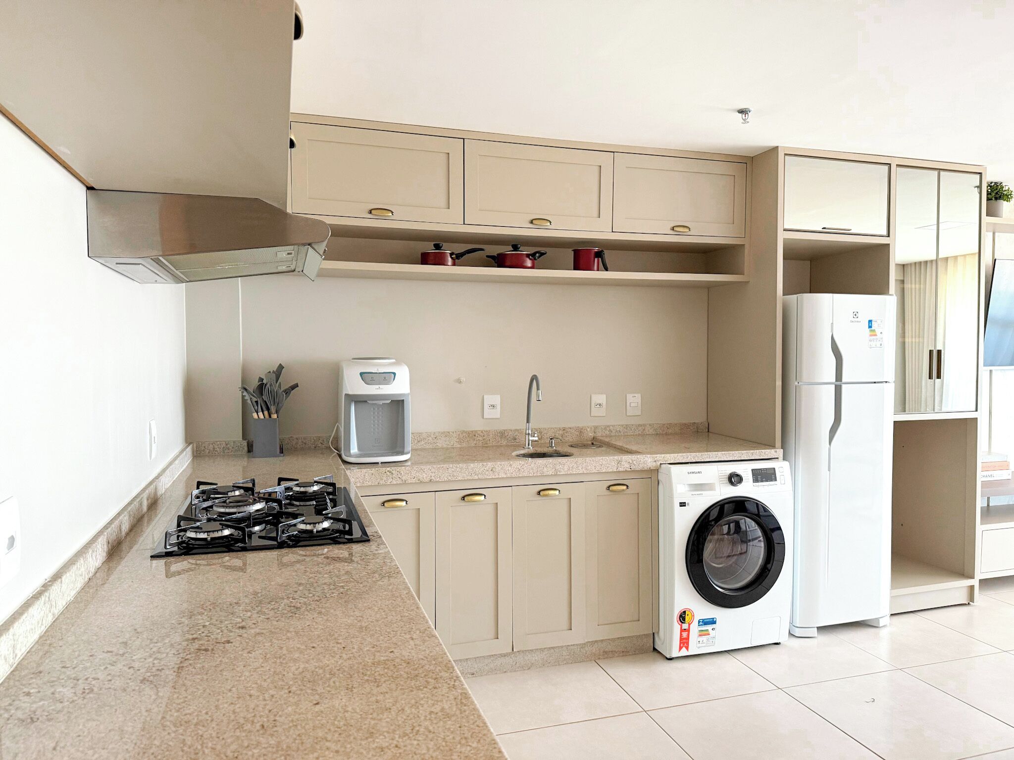 Une cuisine compacte équipée d’une cuisinière à gaz, d’une machine à café, d’un lave-linge et d’un réfrigérateur.