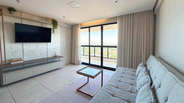 A modern living room with a large window, a flat-screen TV mounted on a marble wall, a grey sofa, and a small coffee table. - STAY Cosmopolitan  (Palmas)