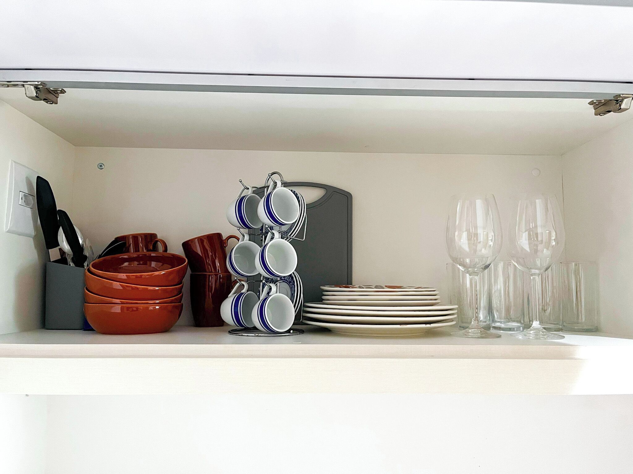 A kitchen shelf with various dishes, including a stack of plates, a rack of cups, and a few bowls.