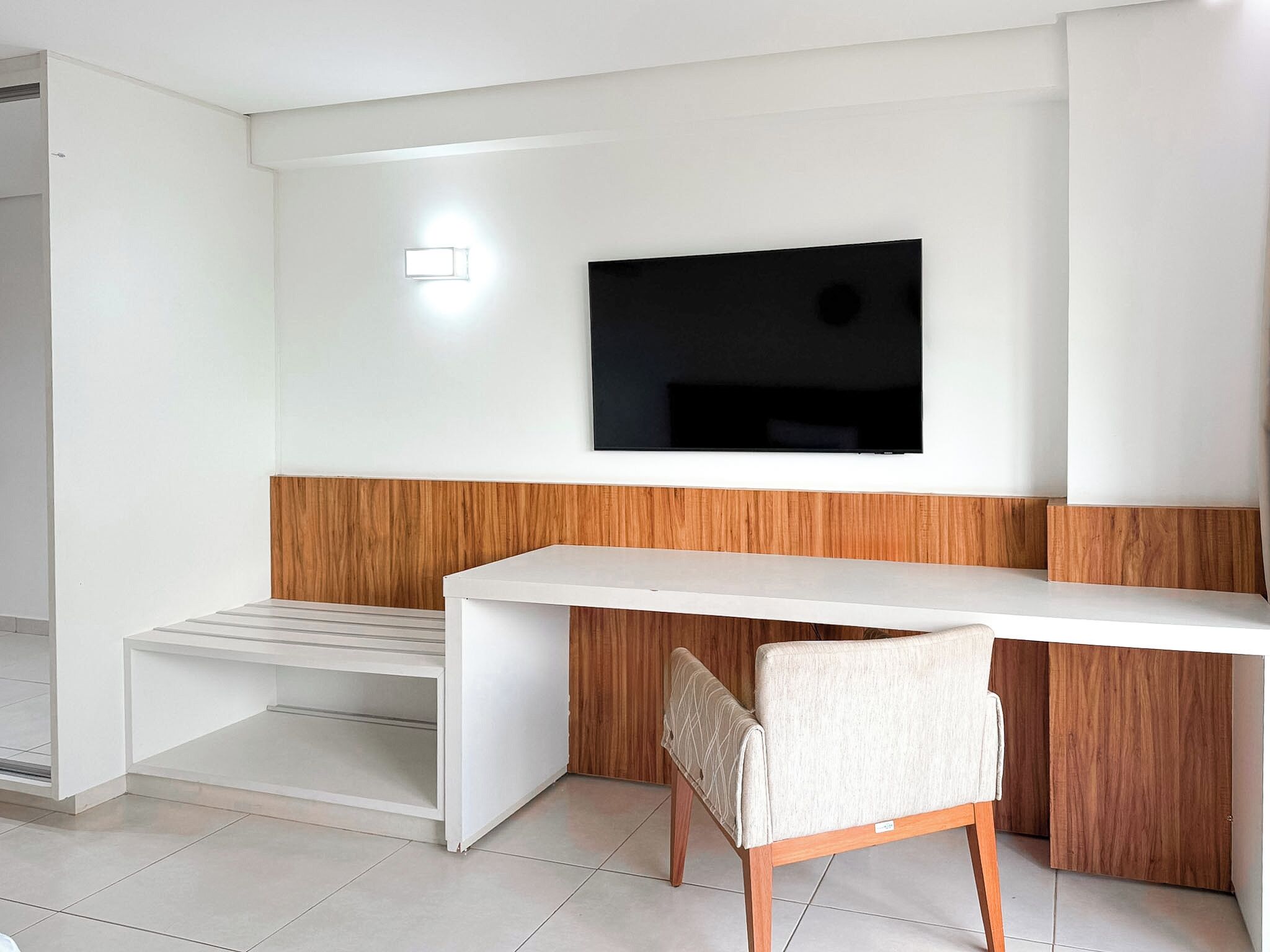 A modern room with a white desk, a chair, a television mounted on the wall, and a wooden accent wall.