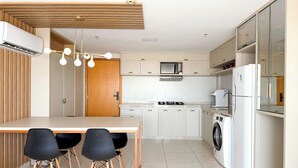 Une cuisine moderne dotée d’un îlot central, de meubles blancs, d  ’un four à micro-ondes, d’une cuisinière, d’un lave-linge et d’un réfrigérateur.