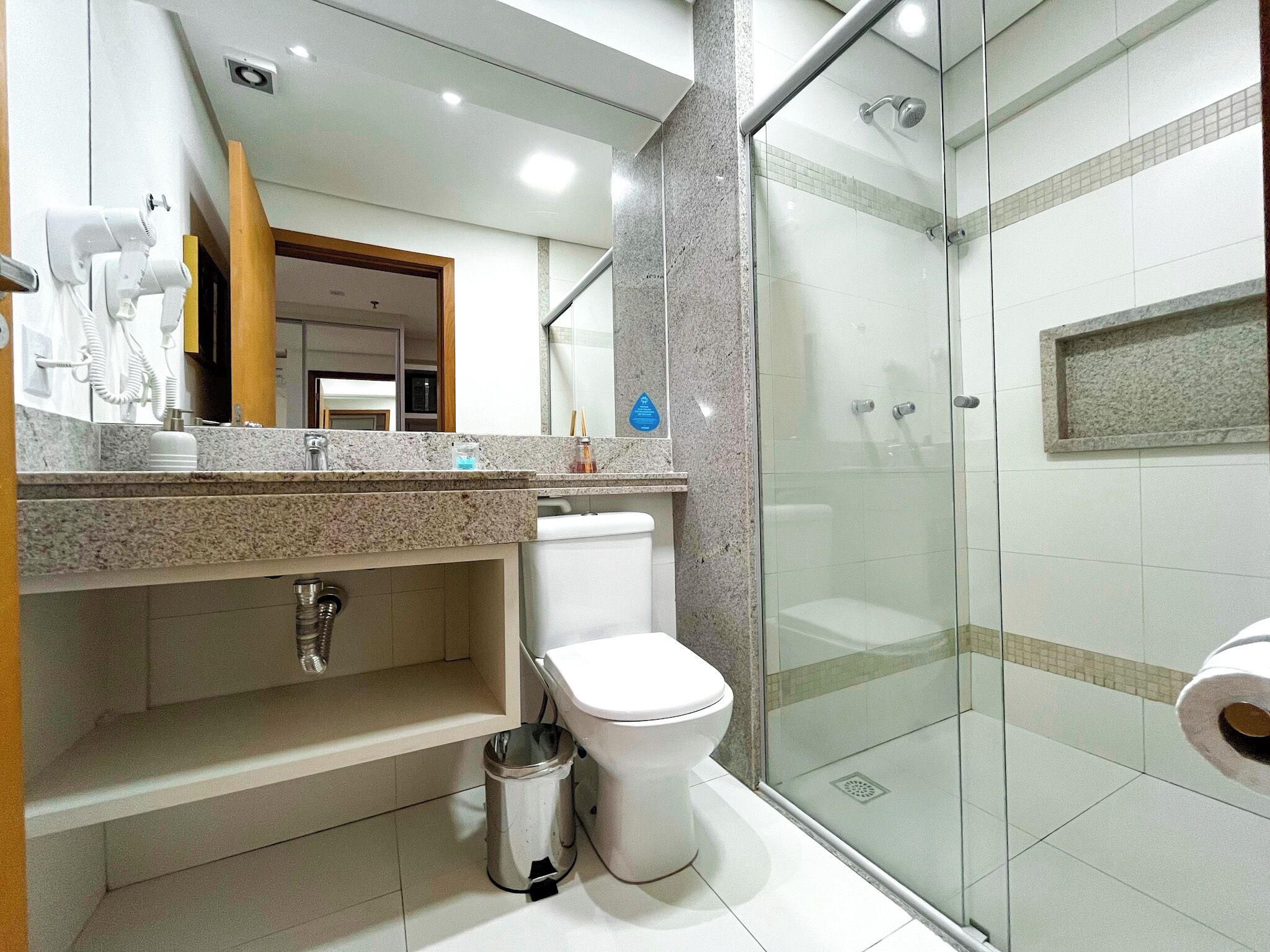 A modern bathroom with a glass-enclosed shower, a toilet, and a sink with a marble countertop.