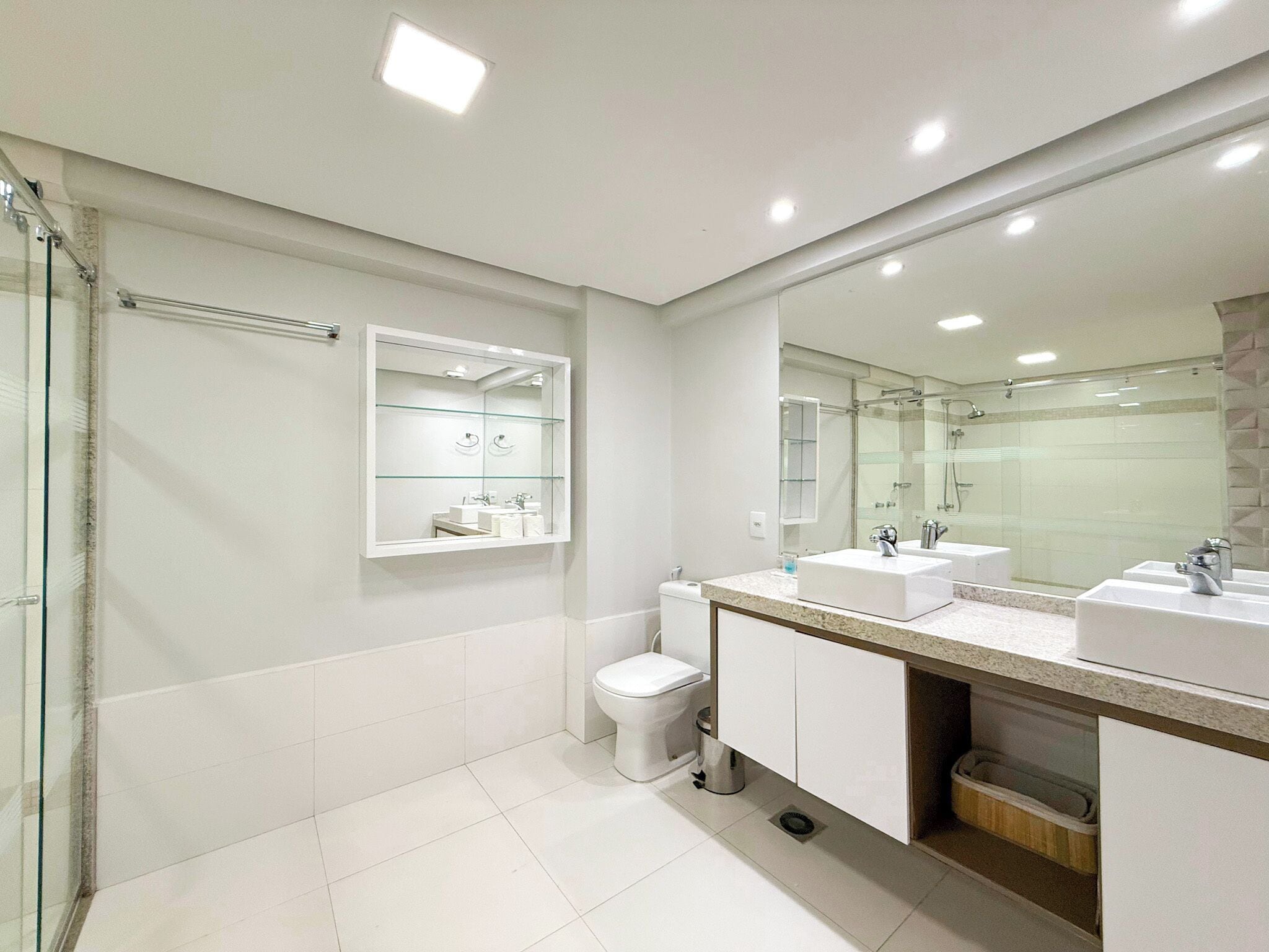 A modern bathroom with two sinks, a toilet, and a glass shower enclosure.