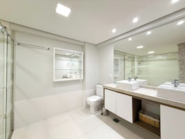 Un baño moderno con dos lavamanos, un inodoro y una cabina de ducha con mampara de vidrio.