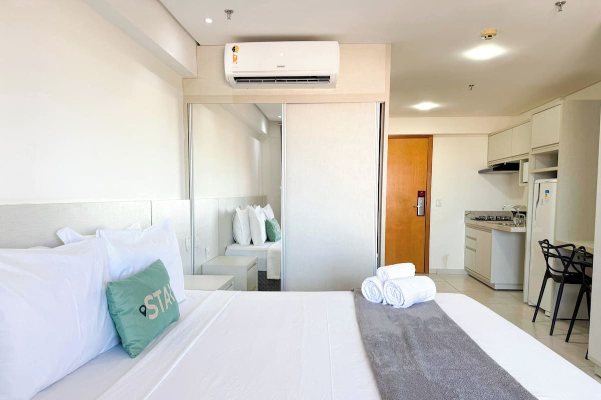 A hotel room with a bed, a small desk, a kitchenette, and a bathroom.