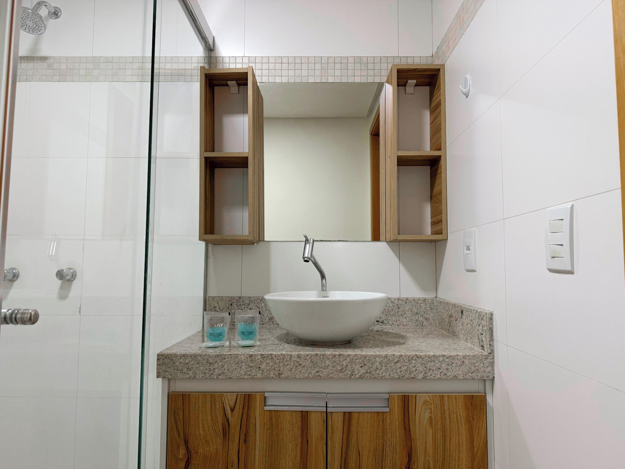 A bathroom with a white sink, wooden cabinets, a mirror, and a shower.