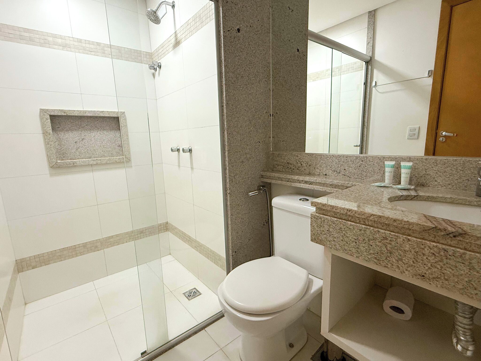 Un baño con cabina de ducha de vidrio, inodoro, lavamanos con artículos de aseo y espejo.