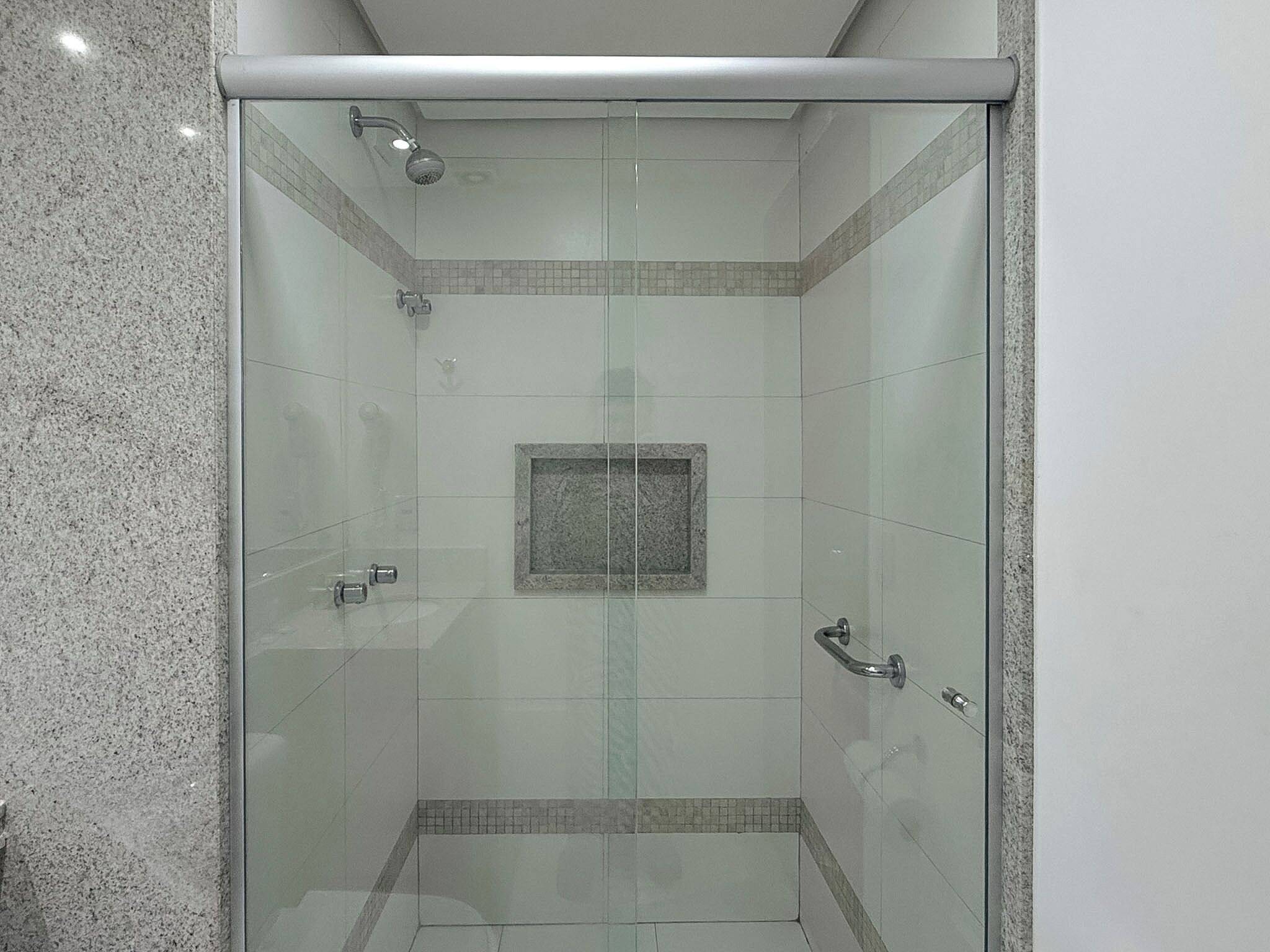 A glass-enclosed shower with a tiled floor and a small square tile decoration on the wall.