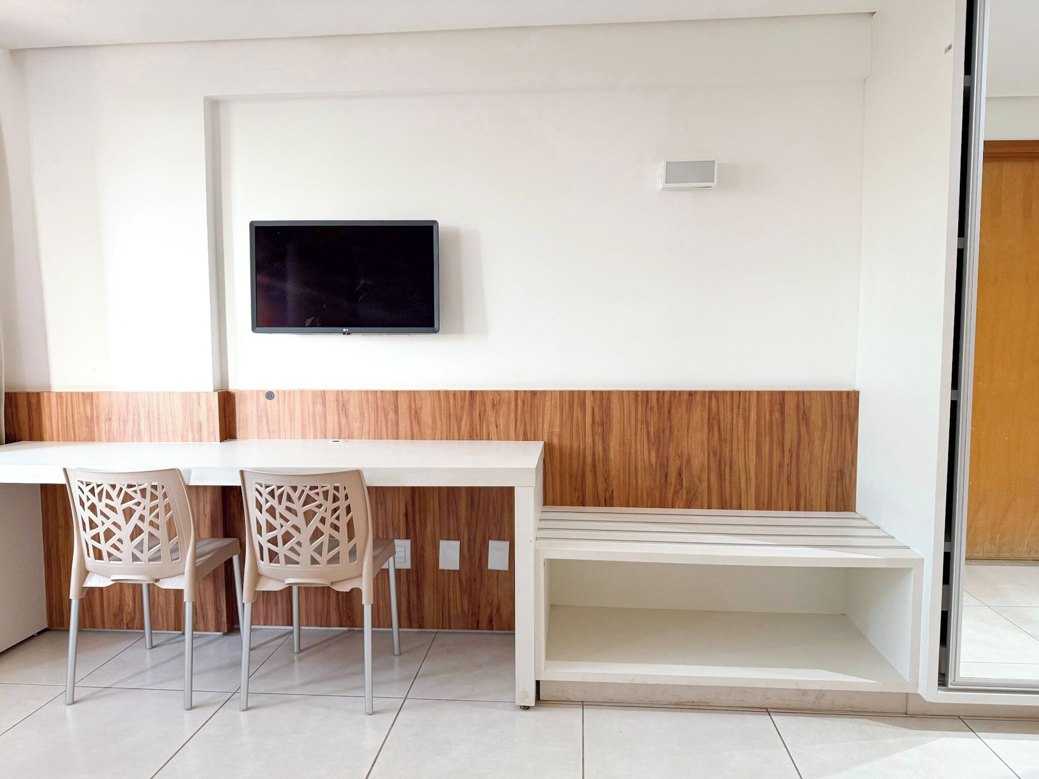 Una habitación moderna con un escritorio blanco, dos sillas, un televisor de pantalla plana montado en la pared y una pared de acento de madera.