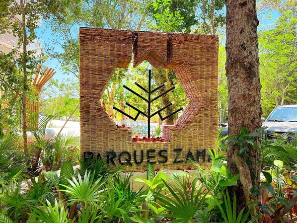 A sign with a tree design and the text "ORQUES ZAM" surrounded by lush greenery.