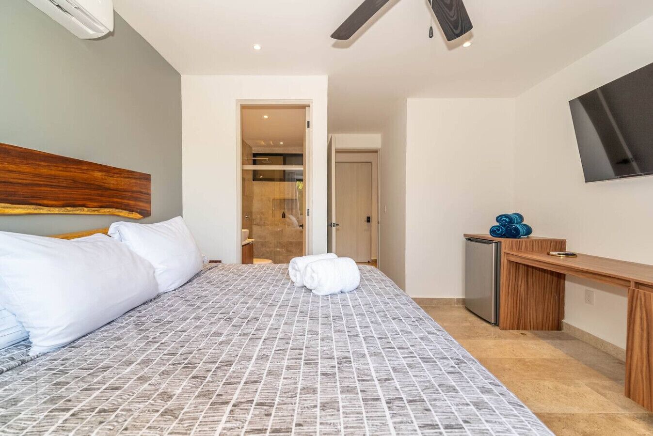 A hotel room with a bed, a desk, a TV, and a shower area.